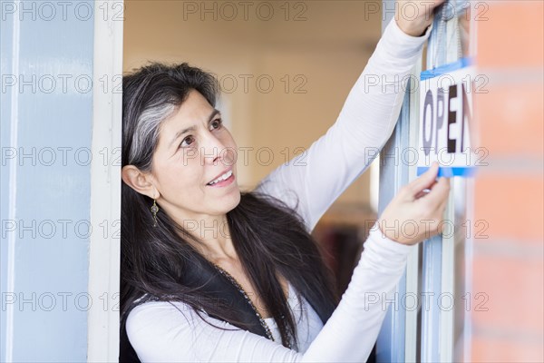 Hispanic small business owner hanging open sign on door