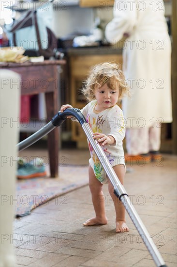 Caucasian baby boy vacuuming in kitchen