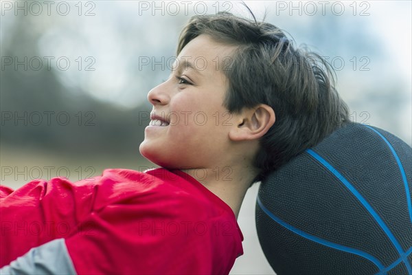 Caucasian boy laying on basketball outdoors