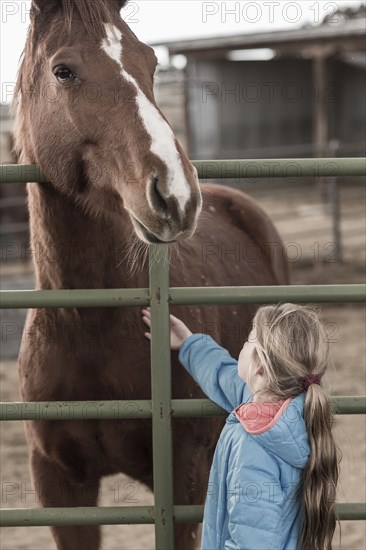 Caucasian girl petting horse on ranch