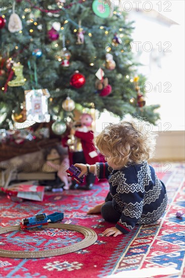 Caucasian baby boy playing with toys under Christmas tree