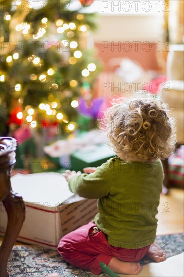 Caucasian baby boy opening presents near Christmas tree