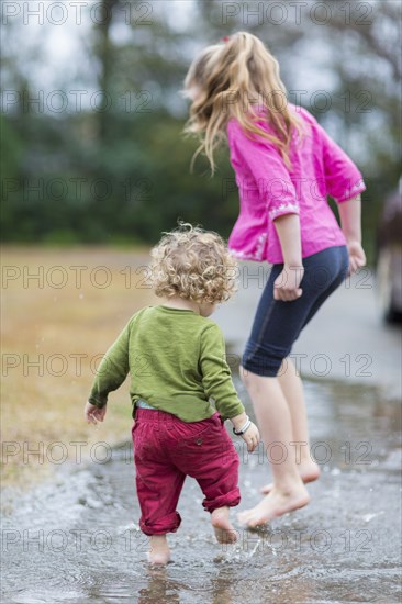 Caucasian children splashing in puddle