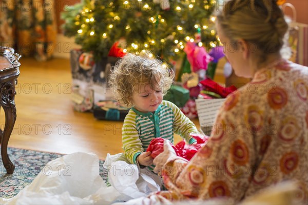 Caucasian mother and baby son opening presents near Christmas tree