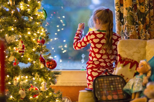 Caucasian girl looking out window near Christmas tree