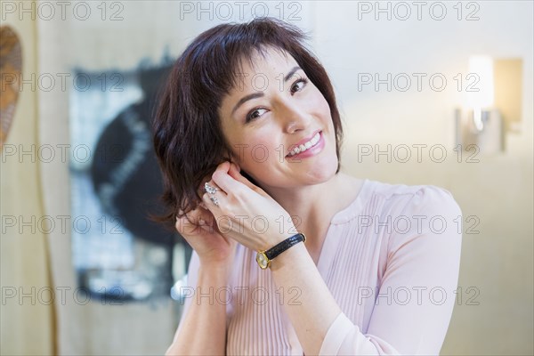 Hispanic woman putting on earrings in mirror