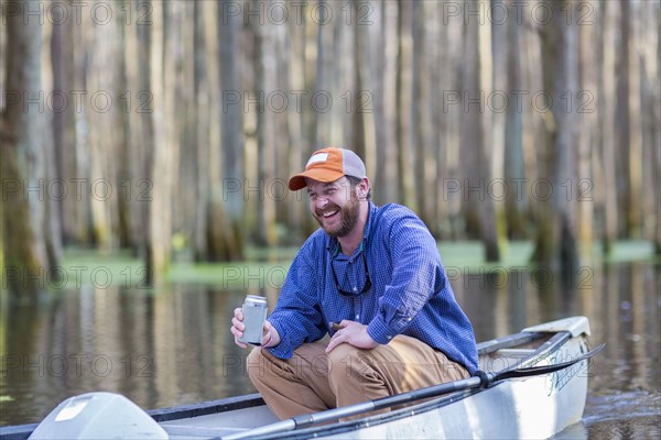 Caucasian man drinking beer in canoe on river