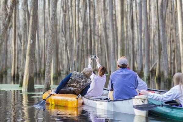 Caucasian family taking cell phone photographs in canoes on river