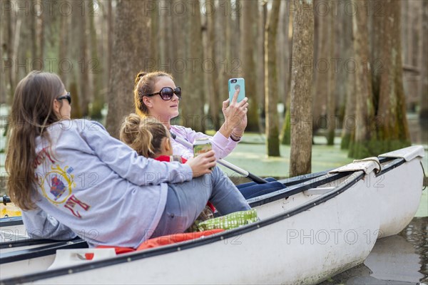Caucasian family taking cell phone photographs in canoes on river