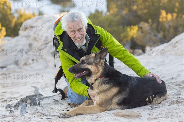 Older man petting dog on rocky hillside