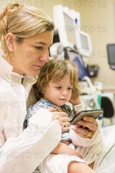 Caucasian mother and son texting on cell phone in hospital