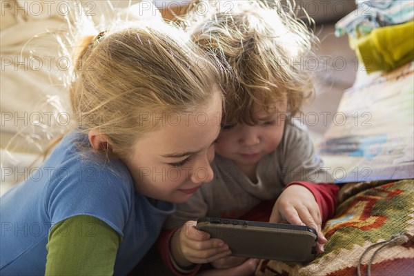 Caucasian brother and sister using cell phone on sofa