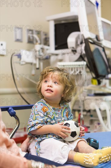 Caucasian boy sitting on hospital bed with soccer ball