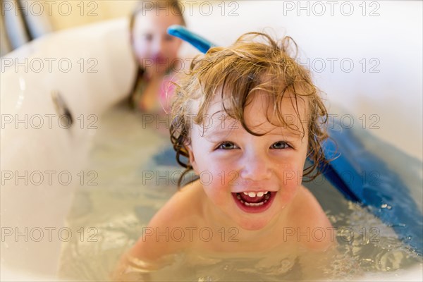 Caucasian children playing with mermaid tail in bath