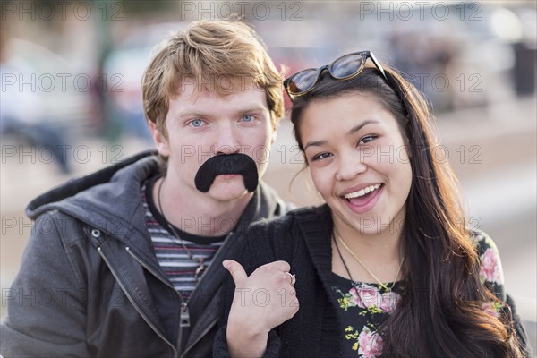 Teenage couple playing with fake mustache