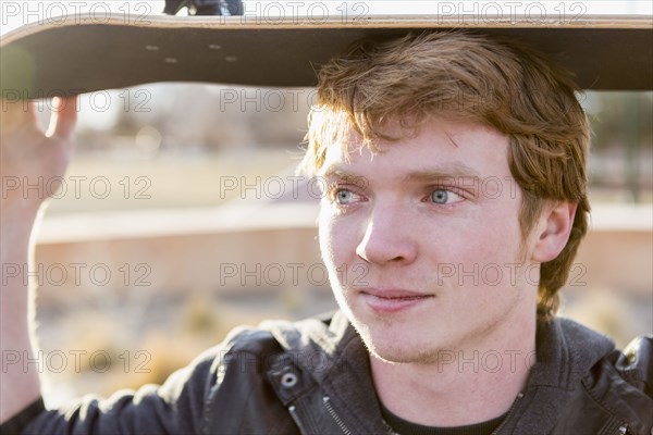 Caucasian teenage boy holding skateboard outdoors