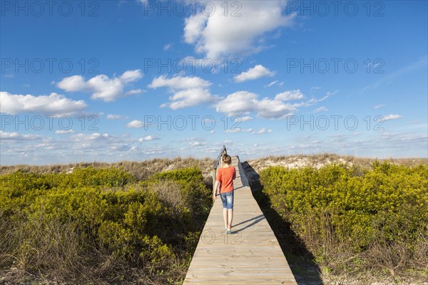 Caucasian girl walking on wooden walkway in remote field