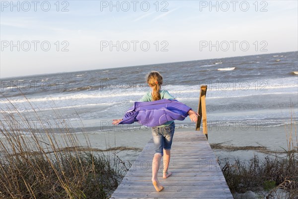 Caucasian girl walking on wooden walkway to beach