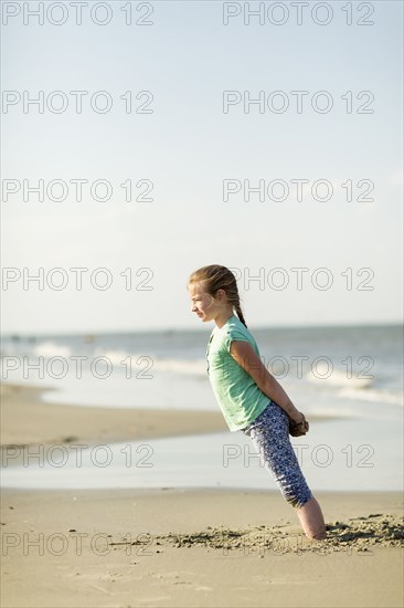 Caucasian girl leaning in sand on beach