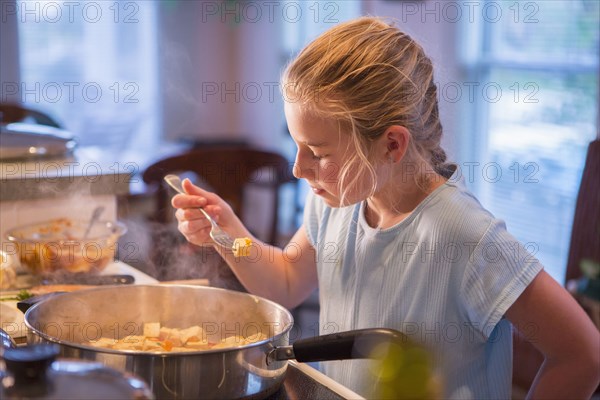 Caucasian girl tasting food and cooking in kitchen