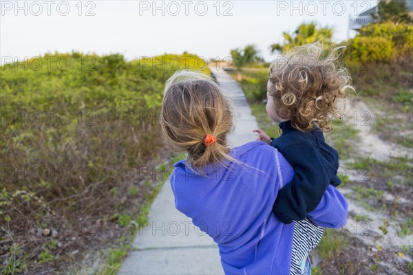 Caucasian girl carrying baby brother on wooden walkway