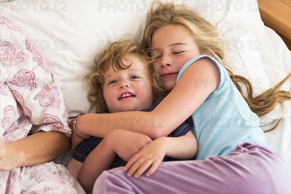 Caucasian brother and sister cuddling on bed