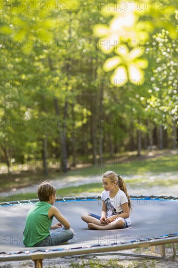 Caucasian children sitting on trampoline