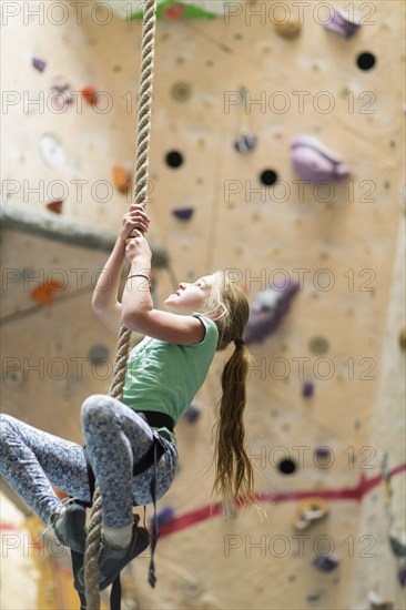 Caucasian girl climbing rope on rock wall indoors