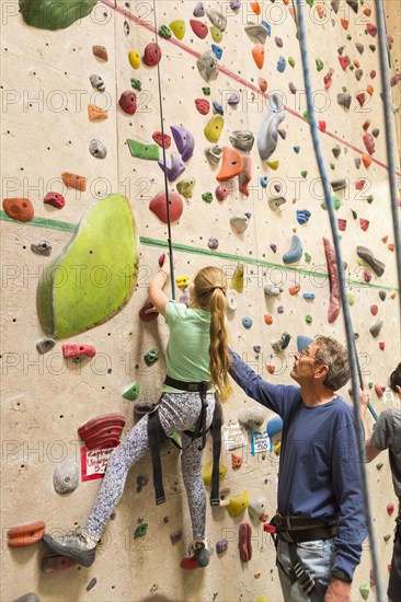 Caucasian father helping daughter climb rock wall indoors