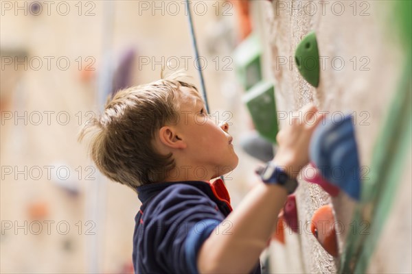 Caucasian boy climbing rock wall indoors