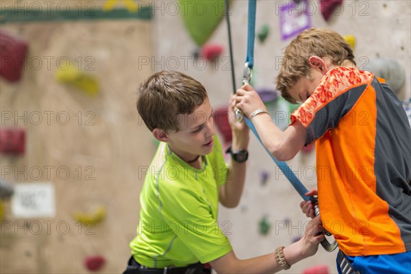 Caucasian boy fastening harness of boy near rock wall