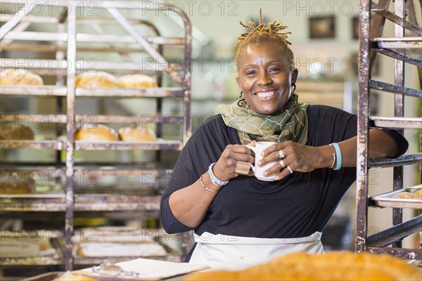 Black baker drinking coffee in bakery kitchen