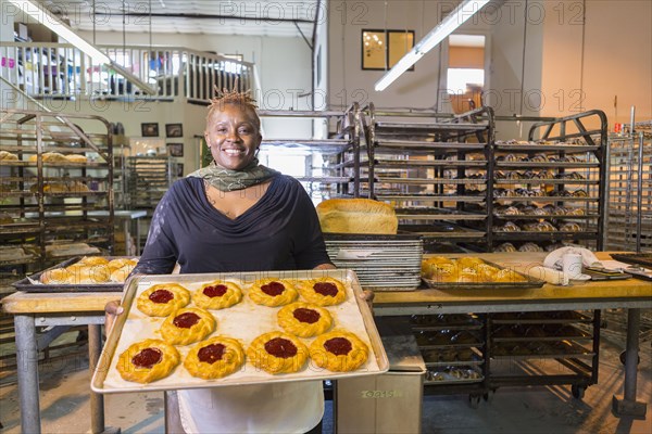 Black baker holding tray of pastries in bakery kitchen