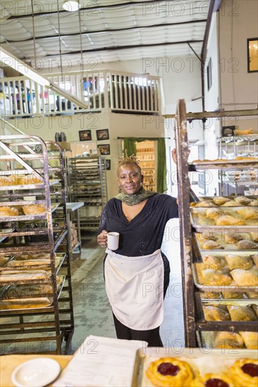 Black baker drinking coffee in bakery kitchen