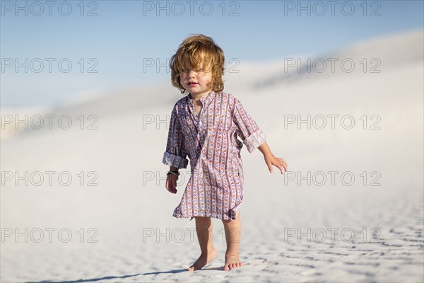 Caucasian baby boy walking on desert sand dune