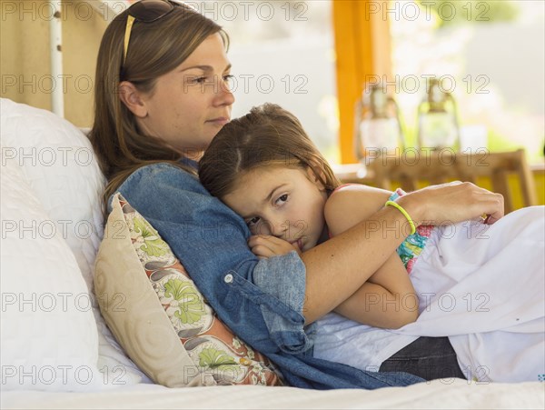 Mother comforting sad daughter on bed