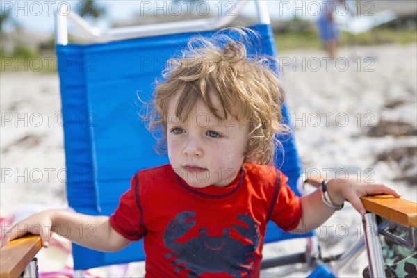 Caucasian baby boy sitting in lawn chair on beach