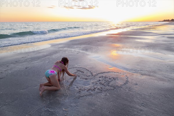 Caucasian girl drawing in sand on beach