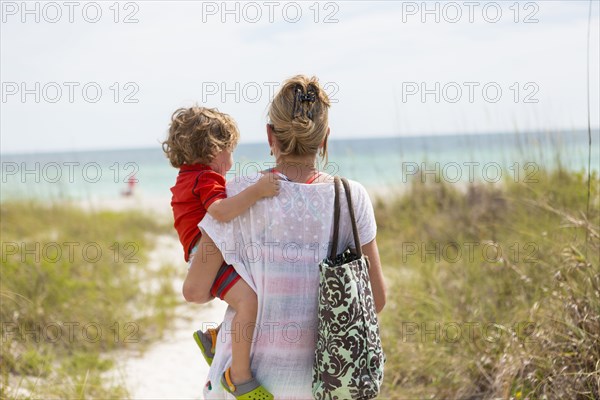 Caucasian mother carrying baby son on beach