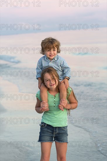 Caucasian girl carrying brother on shoulders on beach