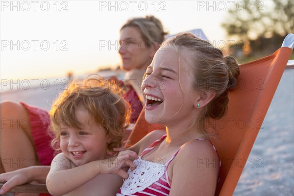 Caucasian children relaxing in lawn chair on beach