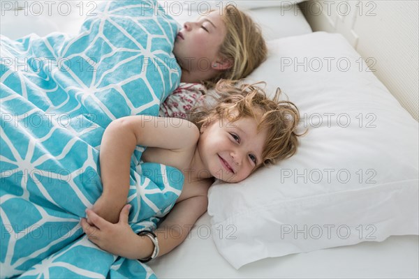 Caucasian brother and sister laying in bed