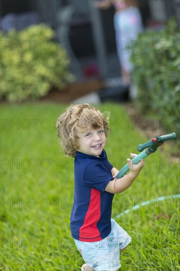 Caucasian baby boy playing with hose in backyard