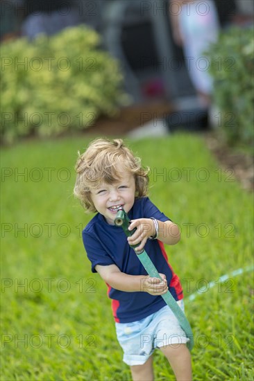 Caucasian baby boy playing with hose in backyard