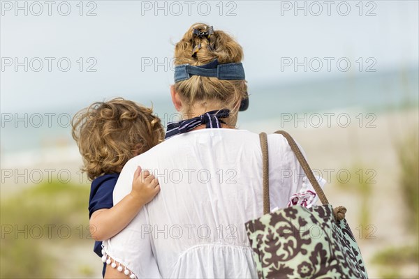 Caucasian mother carrying baby son on beach