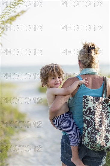 Caucasian mother carrying baby son on beach