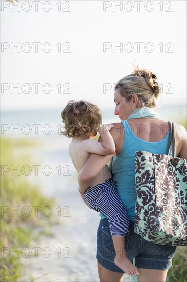 Caucasian mother carrying baby son on beach
