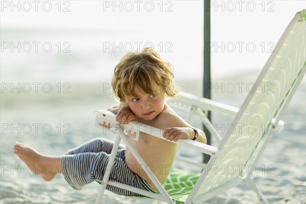 Caucasian baby boy sitting in lawn chair on beach