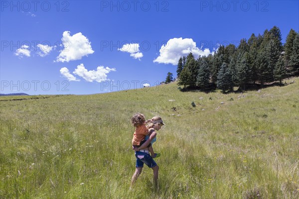 Caucasian girl carrying brother piggyback in field
