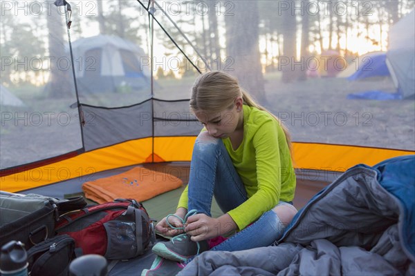 Caucasian girl tying shoes in camping tent